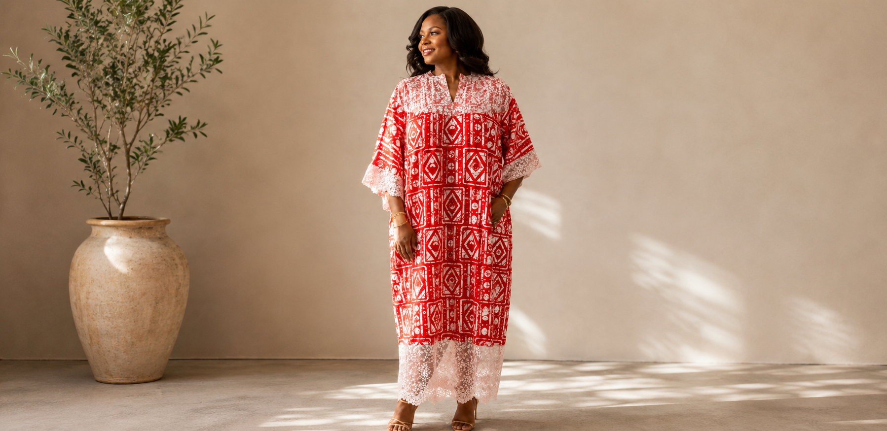 Woman in a red and white patterned dress standing next to a potted plant against a beige wall.